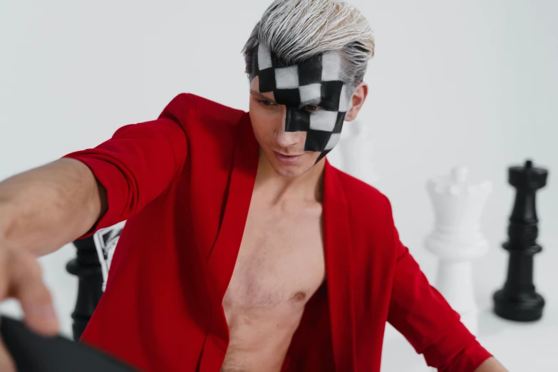 a shirtless man dressed in red stands next to a chessboard and looks at soing out of sight