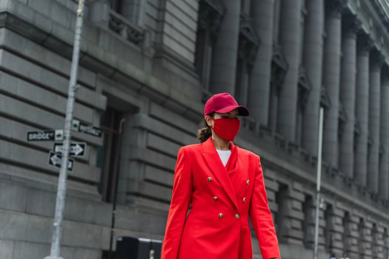 a woman in a red coat and mask walks down the street