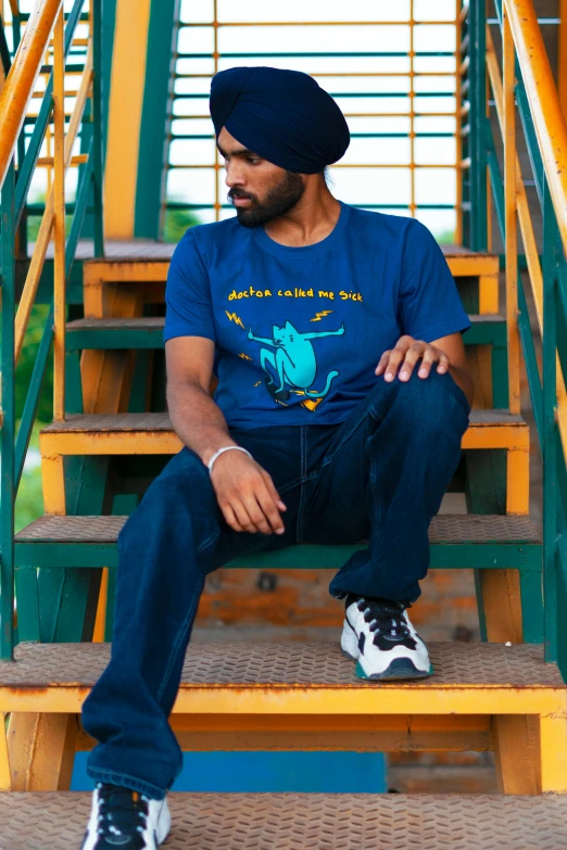 man in blue t - shirt sitting on stairs wearing sneakers and a beanie