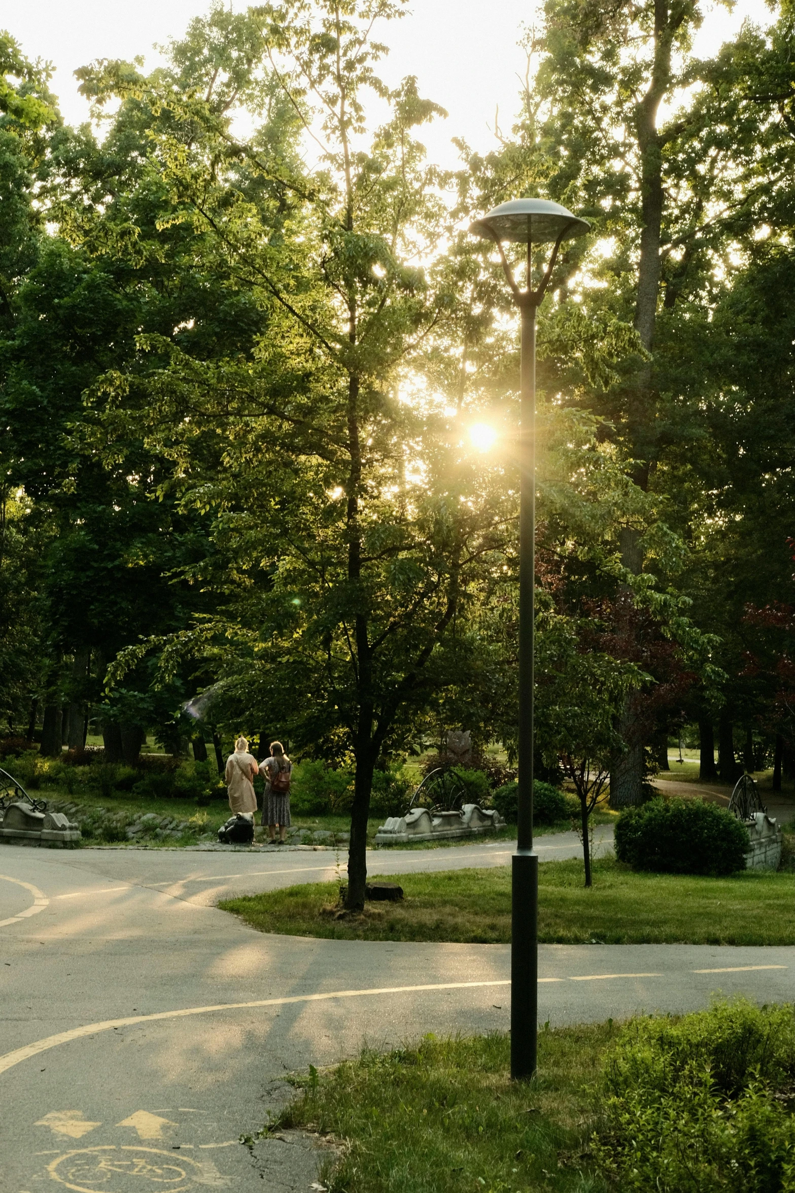 two people are walking on the path through a park