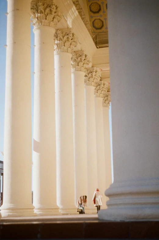 people walking under columns at a building with a clock on top