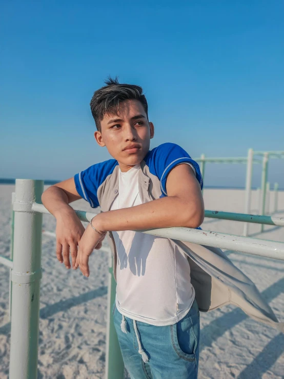 a young man leaning on a fence in front of the beach