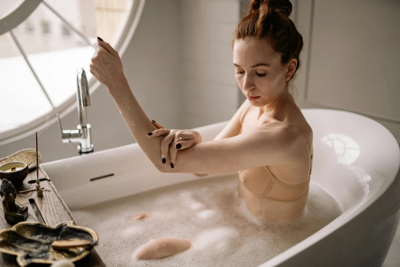 a woman in an incongruct bathtub with  on, removing off her watch