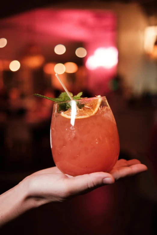 hand holding beverage with straw in it, in a dark room