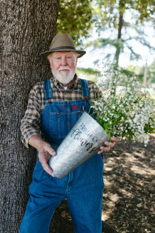 a man with a busher next to a tree and holding a bucket