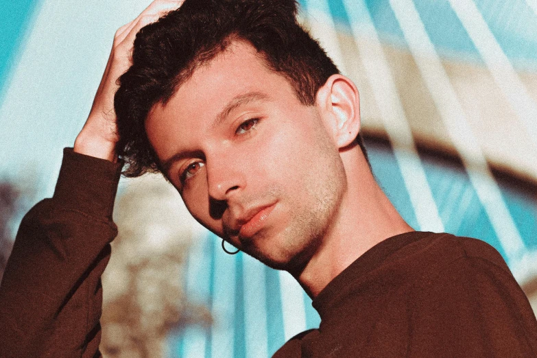 a young man in a brown shirt holding his head with both hands