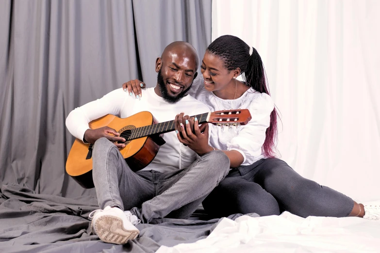 a man and woman smile as they sit together on the floor with a guitar