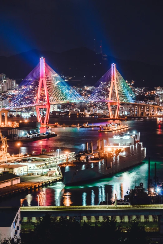 brightly colored lights shine over water as cruise ships pass by