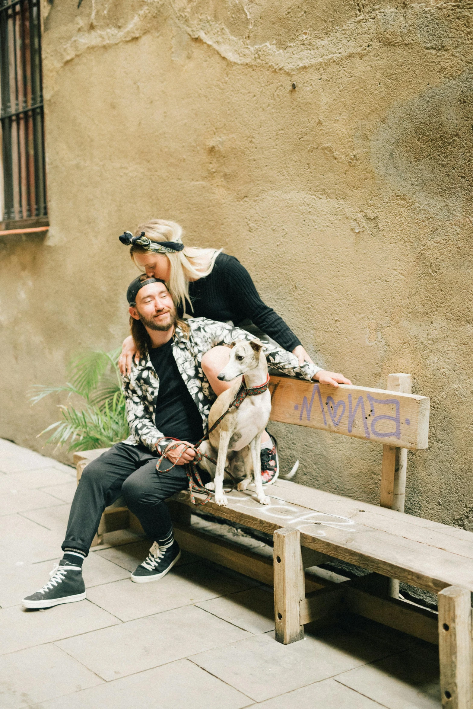 a man sits with his dog on a bench as he kisses a woman