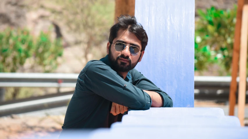 a man with a beard and sunglasses leaning against a pole