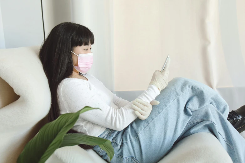 a woman wearing a surgical mask and gloves sitting on a white couch