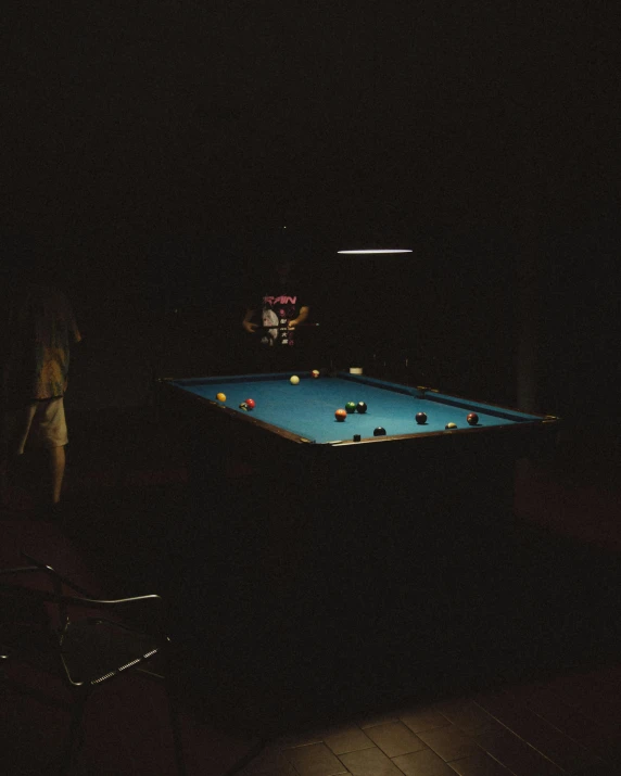 a pool table in a dark room and a person with a racket