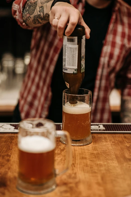 a person pours a beer from a bottle in front of two glasses