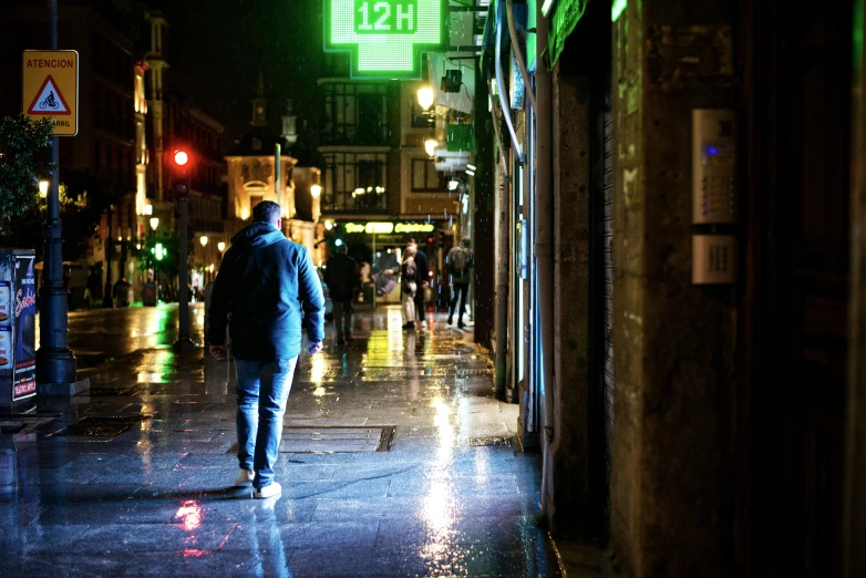 a man walking down the sidewalk at night in the rain