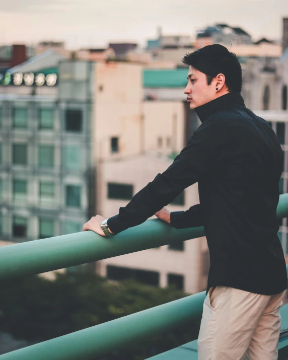 man in black jacket leaning on railing overlooking city
