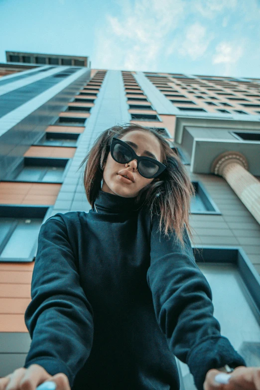 a woman in sunglasses stands in front of a tall building