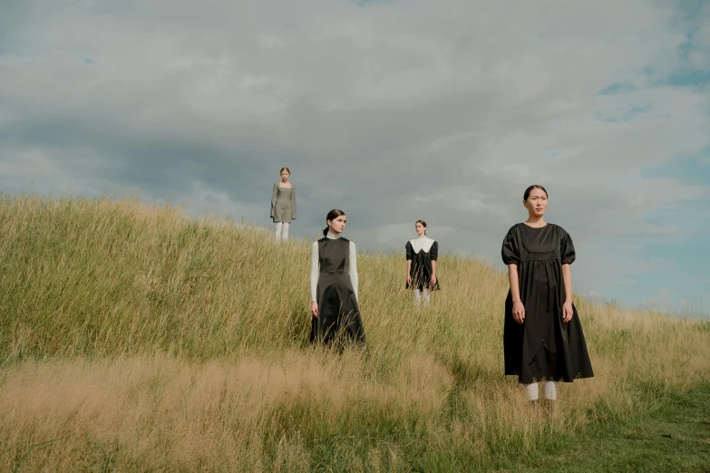 a group of people in black dresses walking in tall grass