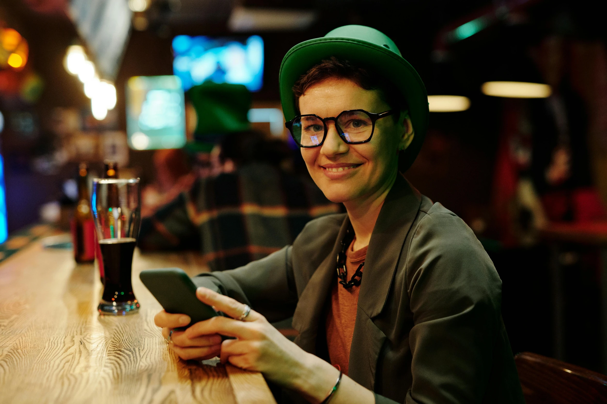 a woman wearing a green hat and glasses smiling at her phone