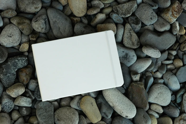 small book laying on rocks with an empty white paper