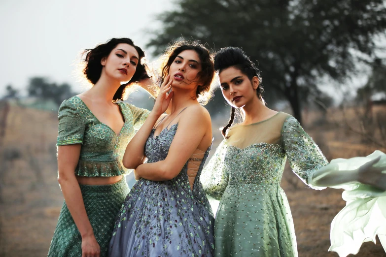 three women standing side by side wearing long dresses