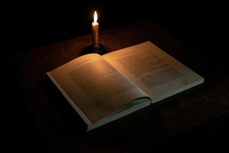 an open book is illuminated by a candle