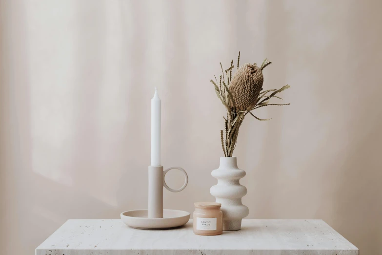 white vase with a flower and a candle siting on a white surface