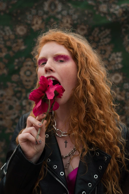 a woman with long red hair holding a flower in her mouth