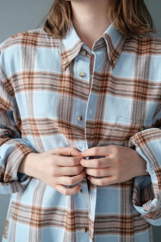 woman wearing a blue plaid shirt has her hands tucked underneath her belt