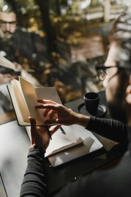 a man is sitting at a table holding an open book