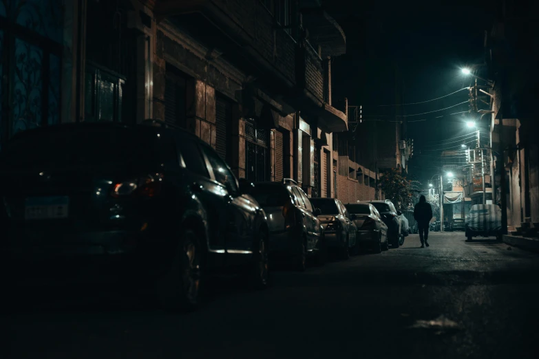 a person walking down a street at night near many parked cars