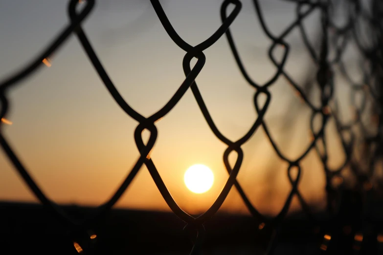 a chain link fence with a sunset in the background