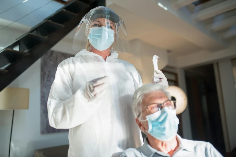 a person in a protective mask wearing a white robe and holding onto another man's head