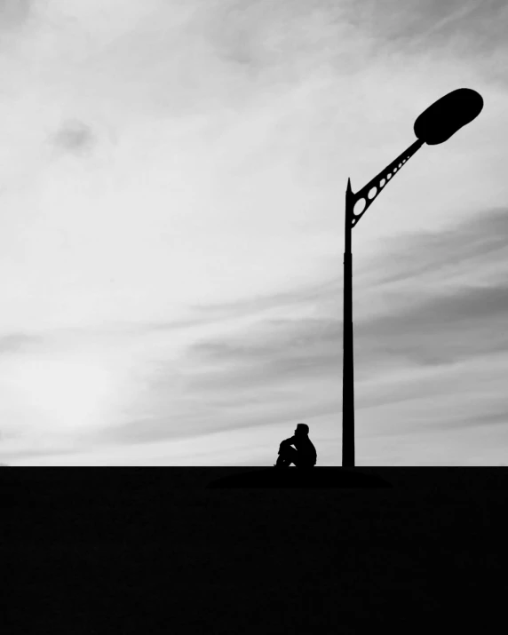 black and white pograph of man sitting on the ground by a street light