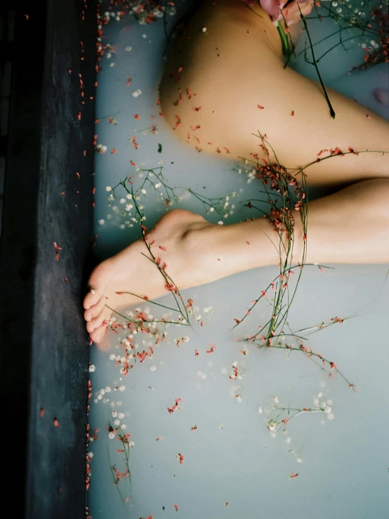 a po of someone laying in a bath tub with flowers growing on it