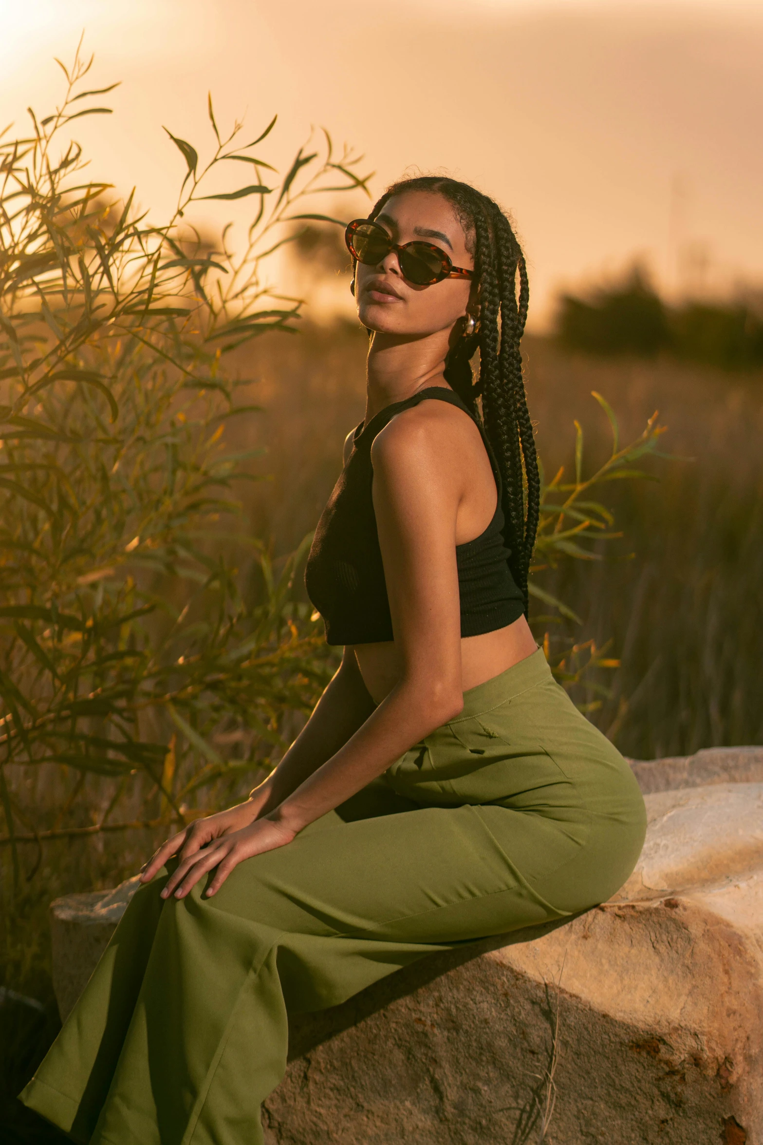 a beautiful woman wearing sunglasses sitting on a rock