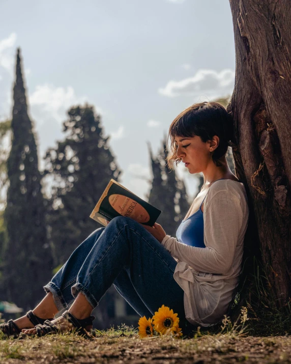 a woman sitting against a tree holding a book