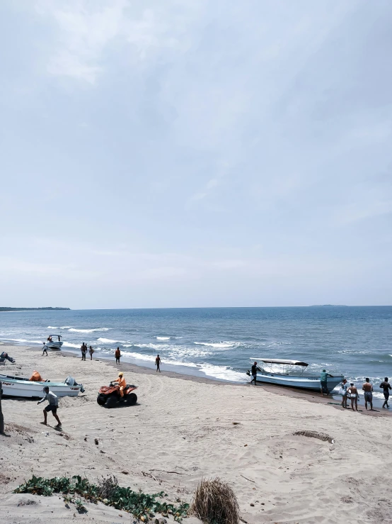 people walking along the beach with some boats