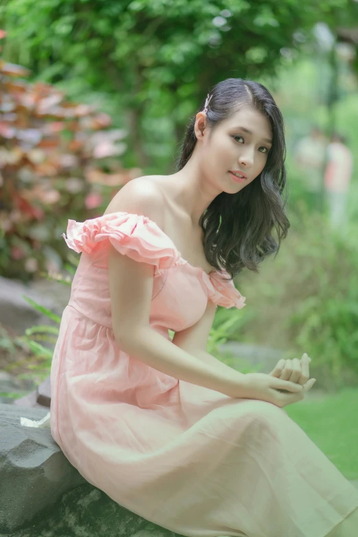 a beautiful asian woman in a pink dress sitting on a rock