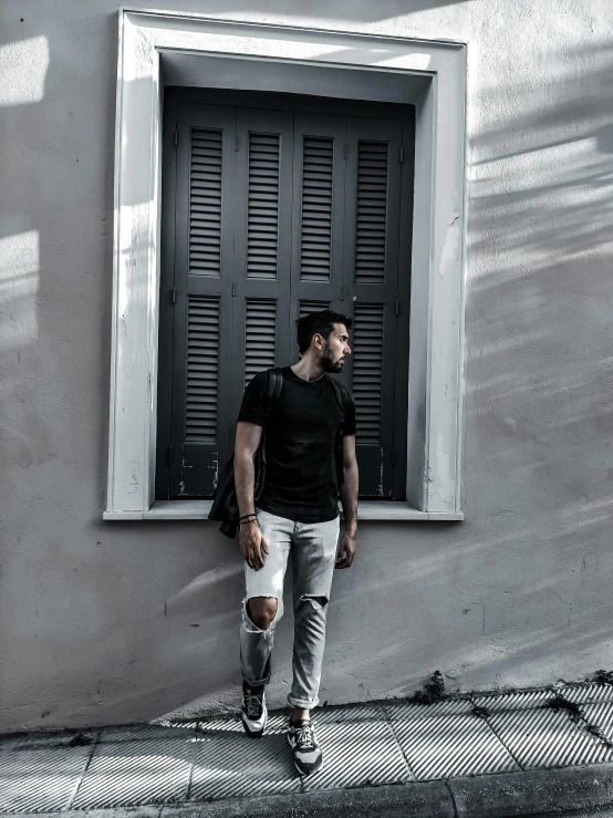 a man in black shirt standing next to window with black shutters