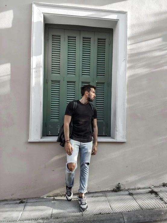 a man is standing near the green shutters on a white wall