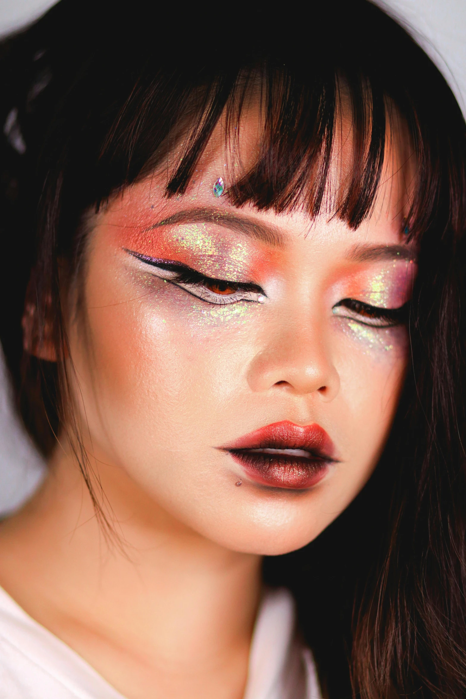 a woman with colorful makeup looks forward at the camera