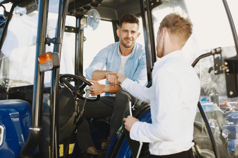 a man drives the tractor with another guy standing nearby