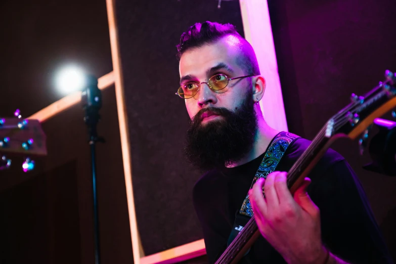 a bearded man is playing the guitar in front of a microphone
