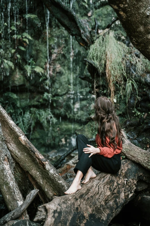 the woman sitting on the log is looking at the water