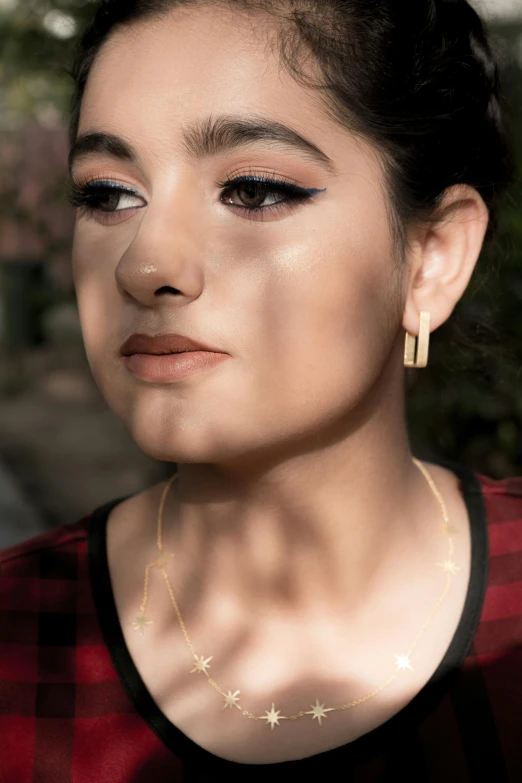 a woman's face wearing black and red top with necklace and gold earring