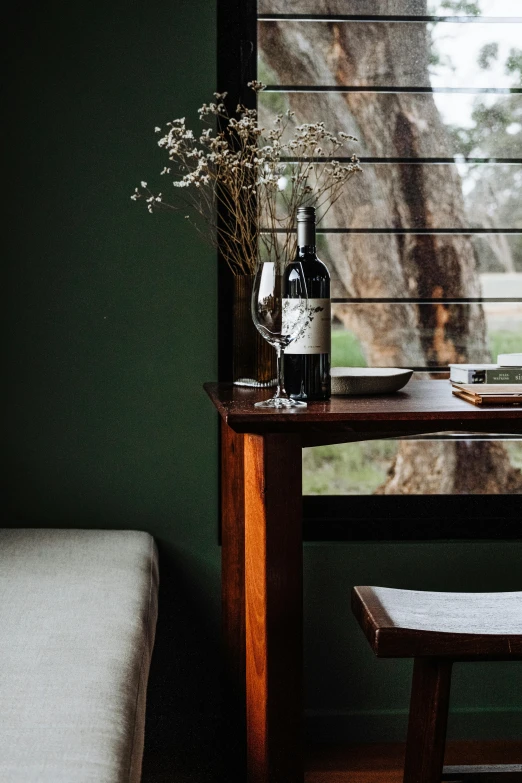 the table in front of the window is empty and has a bottle of alcohol, flowers, and a vase on it