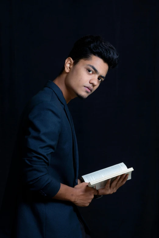 a young man posing holding a book over black background