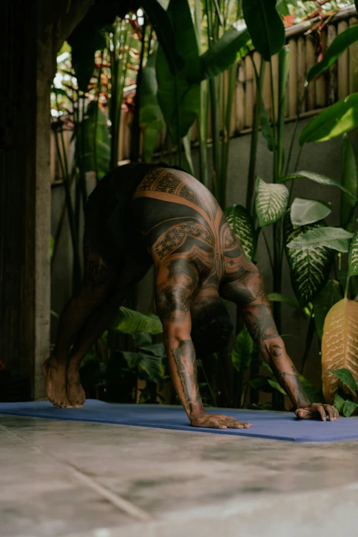 the tattooed man is doing yoga outside near plants