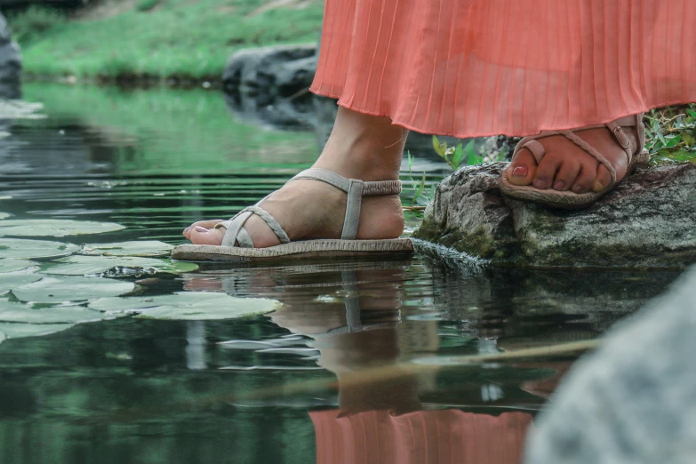 a women's feet wearing sandals while standing near a body of water