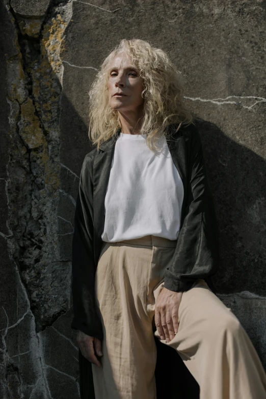 a woman is sitting against a rock and posing for the camera